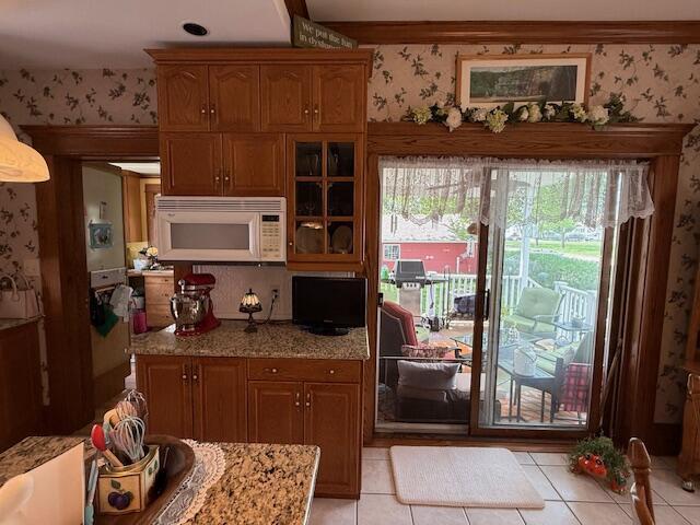 400 S Water St, Sparta, WI 54656 - kitchen featuring white microwave, light tile patterned floors, glass insert cabinets, brown cabinets, and wallpapered walls