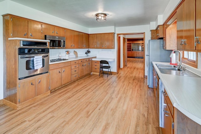 7628 W Mineral Point Rd, Verona, WI 53593 - kitchen with appliances with stainless steel finishes, brown cabinets, light wood-style flooring, a sink, and light countertops