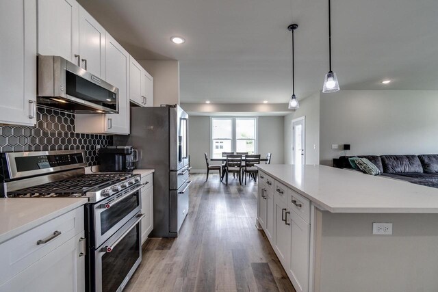 241 E Hubert St, Edgerton, WI 53534 - kitchen featuring appliances with stainless steel finishes, open floor plan, wood finished floors, decorative backsplash, and light countertops