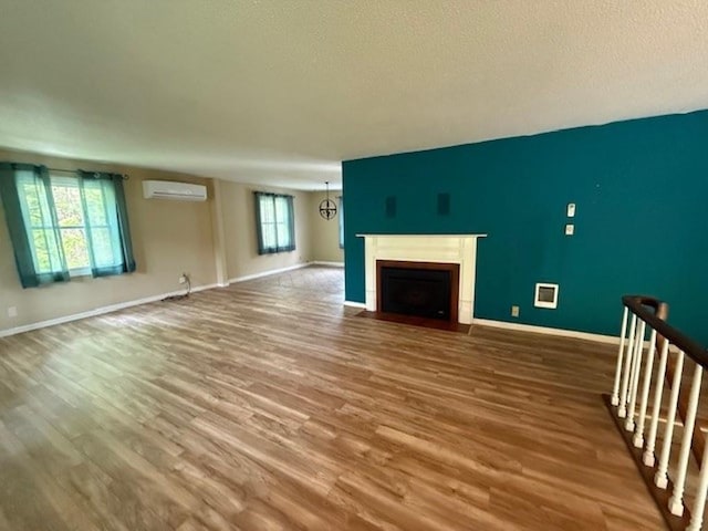 228227 County Road Y, Birnamwood, WI 54414 - unfurnished living room with an AC wall unit, wood finished floors, a fireplace with flush hearth, baseboards, and a textured ceiling