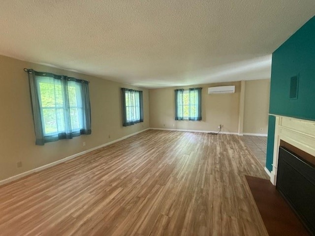 228227 County Road Y, Birnamwood, WI 54414 - unfurnished living room featuring an AC wall unit, a textured ceiling, wood finished floors, a fireplace with flush hearth, and baseboards