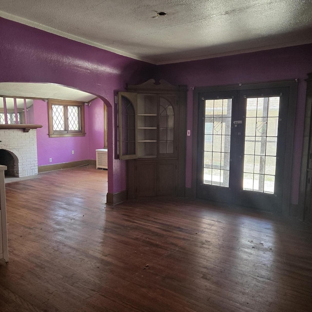 unfurnished living room with wood finished floors, arched walkways, a textured ceiling, french doors, and baseboards