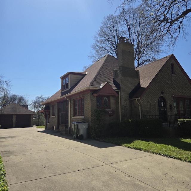 view of side of home with brick siding, a detached garage, an outdoor structure, a chimney, and a shingled roof