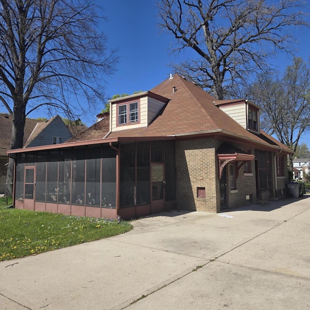 view of side of home featuring a sunroom, brick siding, and a shingled roof