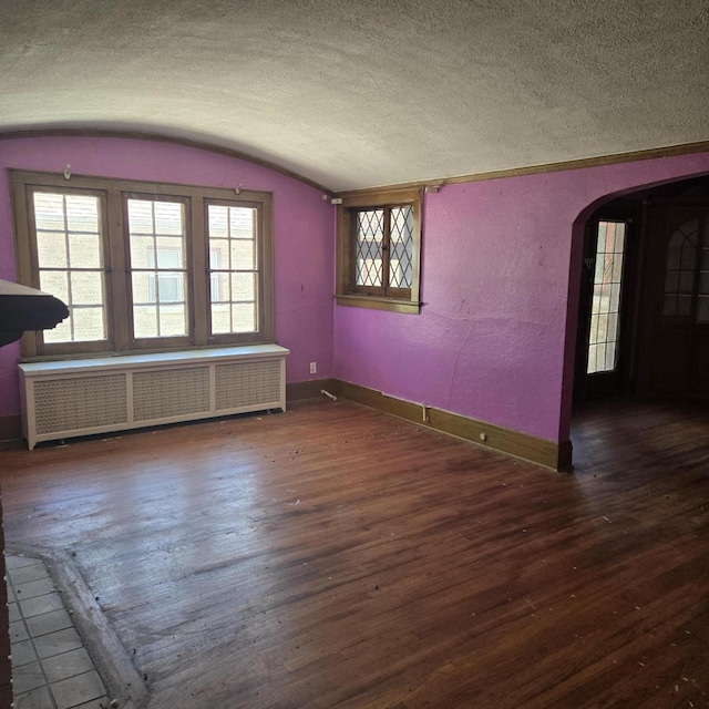 spare room with radiator, baseboards, arched walkways, hardwood / wood-style floors, and a textured ceiling
