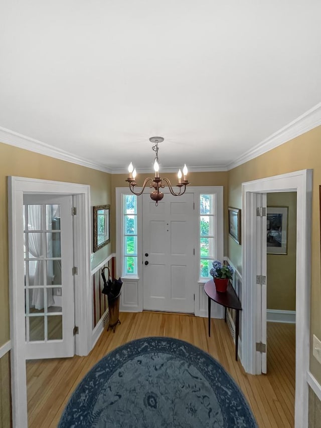 foyer entrance with a chandelier, light wood-style flooring, ornamental molding, and baseboards