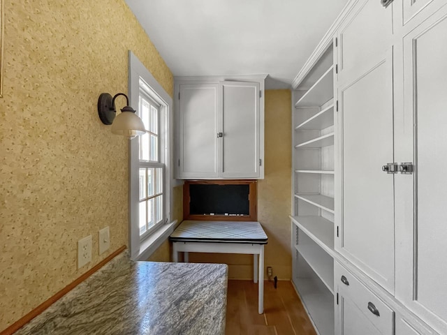 unfurnished office featuring wood finished floors, wallpapered walls, and baseboards