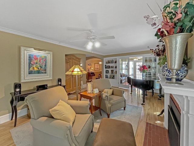 living room featuring a ceiling fan, arched walkways, crown molding, light wood finished floors, and baseboards