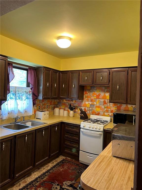 W4670 County Highway F, Springbrook, WI 54875 - kitchen featuring white range with gas cooktop, a sink, dark brown cabinetry, stainless steel microwave, and light countertops
