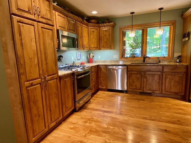 7002 Wildwood Ln, Rhinelander, WI 54501 - kitchen with stainless steel appliances, brown cabinetry, a sink, light wood-style flooring, and decorative light fixtures