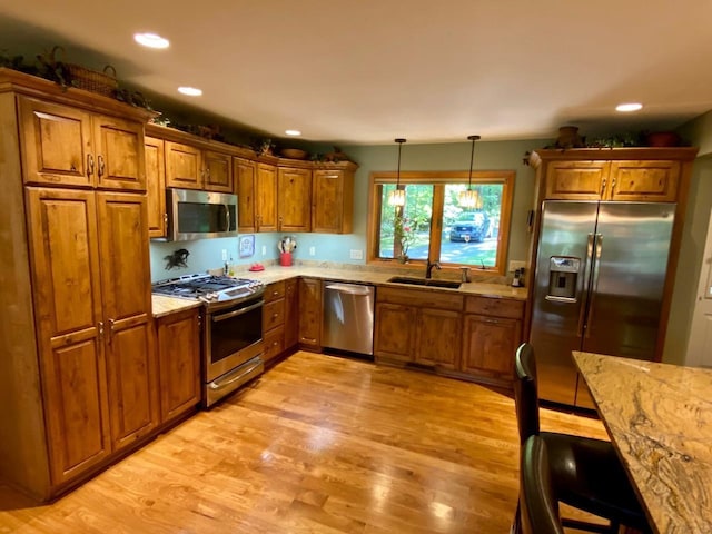 7002 Wildwood Ln, Rhinelander, WI 54501 - kitchen featuring appliances with stainless steel finishes, brown cabinets, light wood finished floors, a sink, and light stone countertops