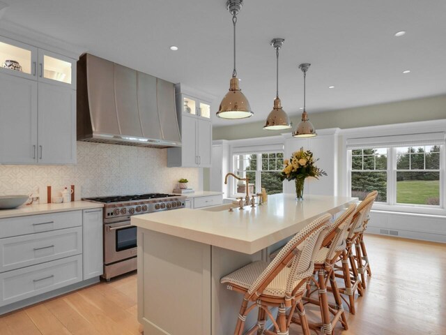 5021 Sherwood Ct, Burlington, WI 53105 - kitchen with high end stove, wall chimney range hood, a sink, light wood-style flooring, and light countertops