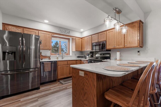 1502 Ridgewood Dr Unit D-7, West Bend, WI 53095 - kitchen featuring appliances with stainless steel finishes, a peninsula, light wood-style flooring, a breakfast bar area, and brown cabinetry