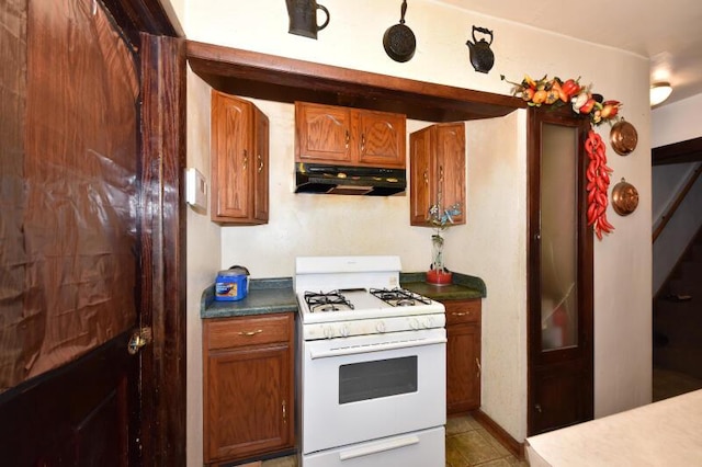 kitchen with under cabinet range hood, white range with gas stovetop, brown cabinetry, and dark countertops