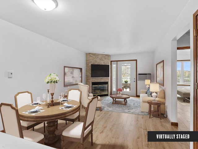 dining space with light wood-style floors, a large fireplace, and a wall mounted air conditioner