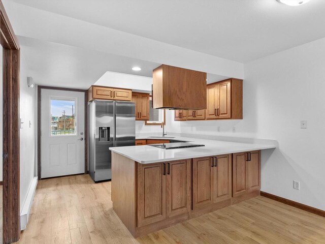 kitchen featuring stainless steel fridge, a peninsula, light wood-style flooring, brown cabinetry, and baseboards