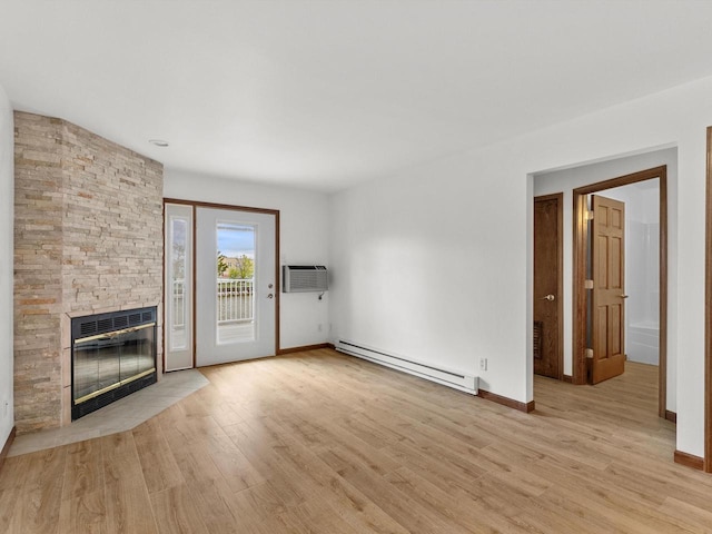 unfurnished living room with baseboard heating, an AC wall unit, light wood finished floors, a stone fireplace, and baseboards