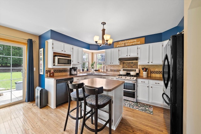 1755 Laura Ln, Port Washington, WI 53074 - kitchen with black appliances, under cabinet range hood, a chandelier, light wood-style floors, and tasteful backsplash