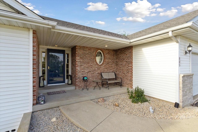 605 E Rime St, Orfordville, WI 53576 - property entrance featuring brick siding, a shingled roof, an attached garage, and a porch