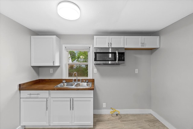 5015 N 25th St, Milwaukee, WI 53209 - kitchen with stainless steel microwave, a sink, baseboards, white cabinetry, and dark countertops