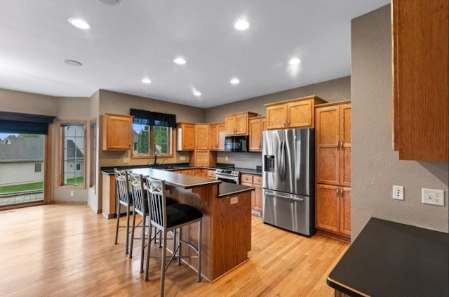 2605 River Ridge Drive, Waukesha, WI 53189 - kitchen featuring stainless steel appliances, dark countertops, a breakfast bar area, recessed lighting, and light wood-type flooring