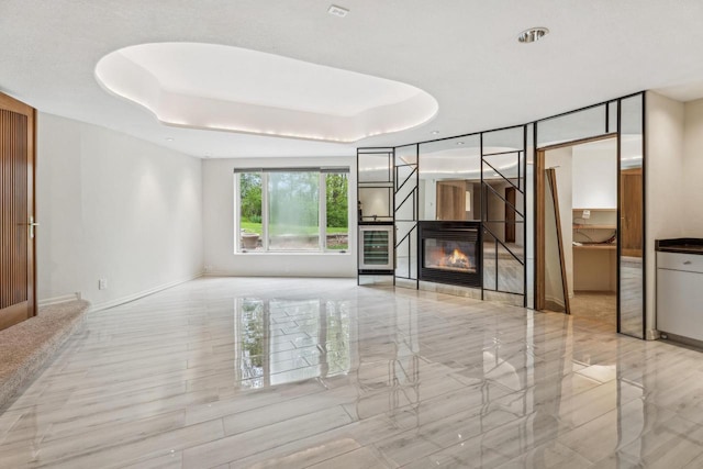 58 Oakridge Ct, Fond Du Lac, WI 54937 - unfurnished living room with a glass covered fireplace, baseboards, a tray ceiling, and wine cooler