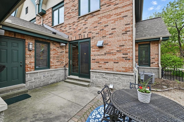 1420 N Astor St, Milwaukee, WI 53202 - doorway to property featuring brick siding, a patio, central air condition unit, roof with shingles, and outdoor dining space