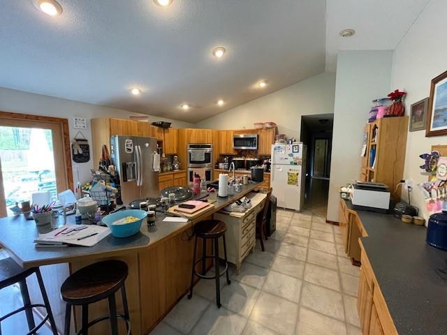13550 W Froemel Rd, Hayward, WI 54843 - kitchen with stainless steel appliances, a breakfast bar, brown cabinetry, vaulted ceiling, and dark countertops