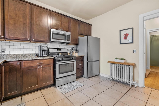 2207 N 51st St, Milwaukee, WI 53208 - kitchen with stainless steel appliances, radiator heating unit, backsplash, light stone counters, and light tile patterned floors