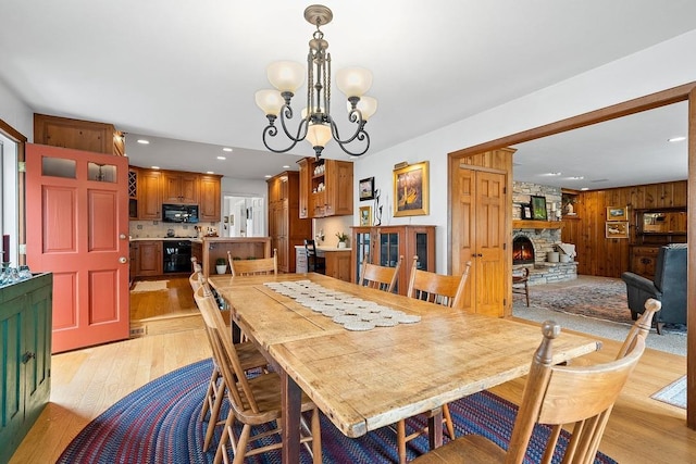 2522 Martha Ave, Green Bay, WI 54301 - dining room featuring light wood-style flooring, a chandelier, recessed lighting, wood walls, and a stone fireplace