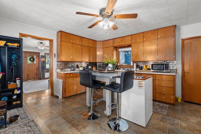 W13491 Reeds Corners Rd, Ripon, WI 54971 - kitchen featuring ceiling fan, brown cabinetry, stainless steel microwave, light countertops, and decorative backsplash