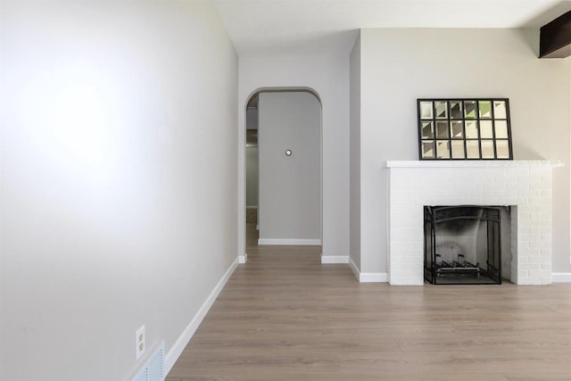 2107 W Grand Ave, Beloit, WI 53511 - unfurnished living room featuring wood finished floors, a fireplace, baseboards, and arched walkways