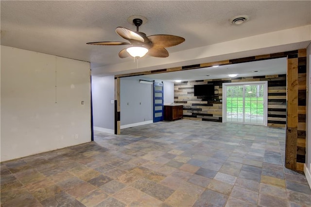 8054 223rd St, Cadott, WI 54727 - unfurnished living room featuring stone finish flooring, a textured ceiling, ceiling fan, a barn door, and baseboards