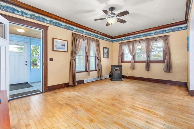 25 E 1st St, Clintonville, WI 54929 - empty room featuring a wood stove, ceiling fan, light wood-style floors, baseboards, and crown molding