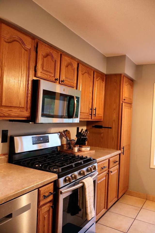 811 Spruce Dr, La Crescent, MN 55947 - kitchen with appliances with stainless steel finishes, light countertops, brown cabinetry, light tile patterned flooring, and baseboards
