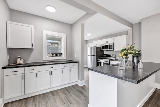 60 Brix St, Clintonville, WI 54929 - kitchen featuring appliances with stainless steel finishes, light wood-style flooring, dark countertops, white cabinets, and a peninsula