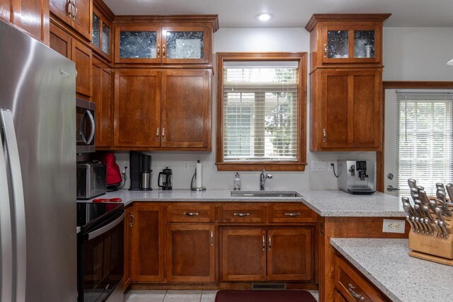 141 Cavil Way, De Pere, WI 54115 - kitchen with appliances with stainless steel finishes, a sink, brown cabinets, light stone countertops, and glass insert cabinets