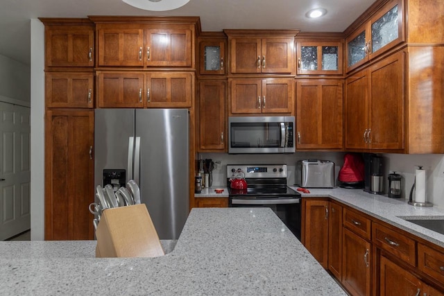 141 Cavil Way, De Pere, WI 54115 - kitchen with appliances with stainless steel finishes, brown cabinets, light stone counters, and glass insert cabinets