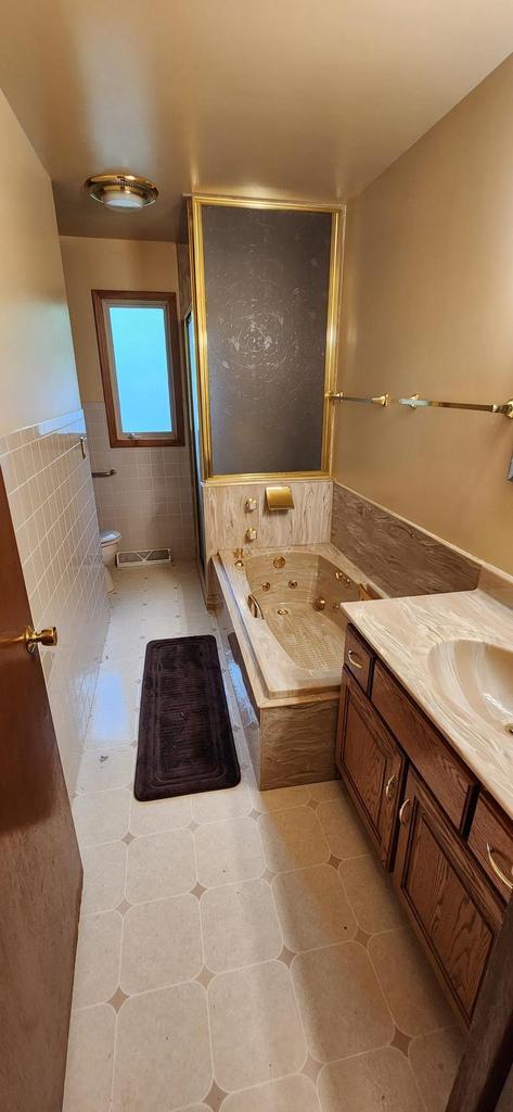 3315 N 12th St, Wausau, WI 54403 - full bath with vanity, a tub with jets, toilet, tile patterned floors, and tile walls