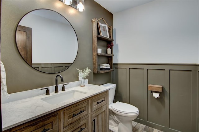 N1816 950th St, Eau Claire, WI 54701 - bathroom with toilet, vanity, a wainscoted wall, wood finished floors, and a decorative wall