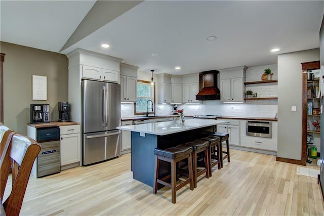 N1816 950th St, Eau Claire, WI 54701 - kitchen featuring stainless steel appliances, custom range hood, a kitchen breakfast bar, decorative backsplash, and light wood finished floors