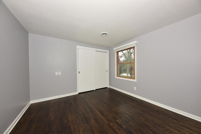 1429 W River Oaks Ln, Mequon, WI 53092 - unfurnished bedroom with baseboards, dark wood-style flooring, and a closet