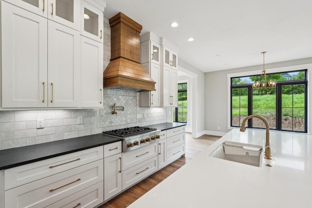 N67W27095 Fanad Dr, Lisbon, WI 53089 - kitchen with a sink, stainless steel gas cooktop, custom range hood, backsplash, and white cabinetry