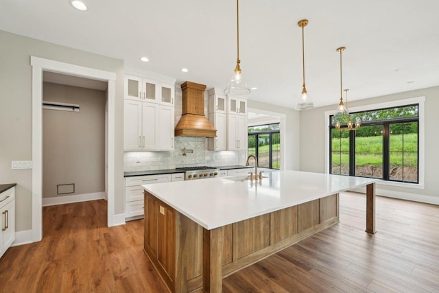 N67W27095 Fanad Dr, Lisbon, WI 53089 - kitchen featuring premium range hood, a sink, backsplash, a large island, and wood finished floors