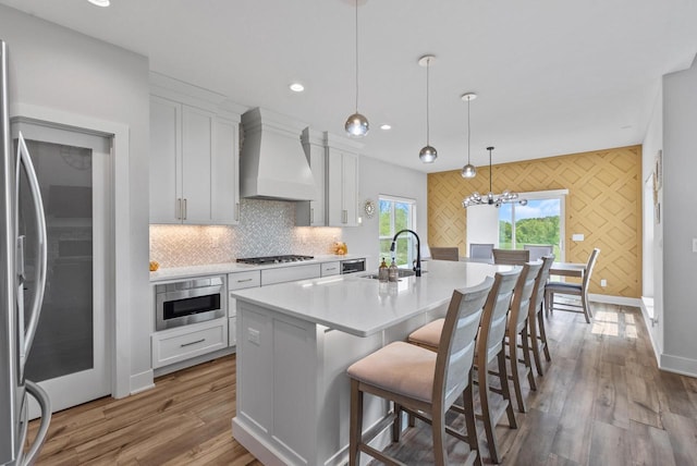 6340 Congress Dr, West Bend, WI 53095 - kitchen featuring wall chimney exhaust hood, a sink, appliances with stainless steel finishes, white cabinetry, and a kitchen island with sink