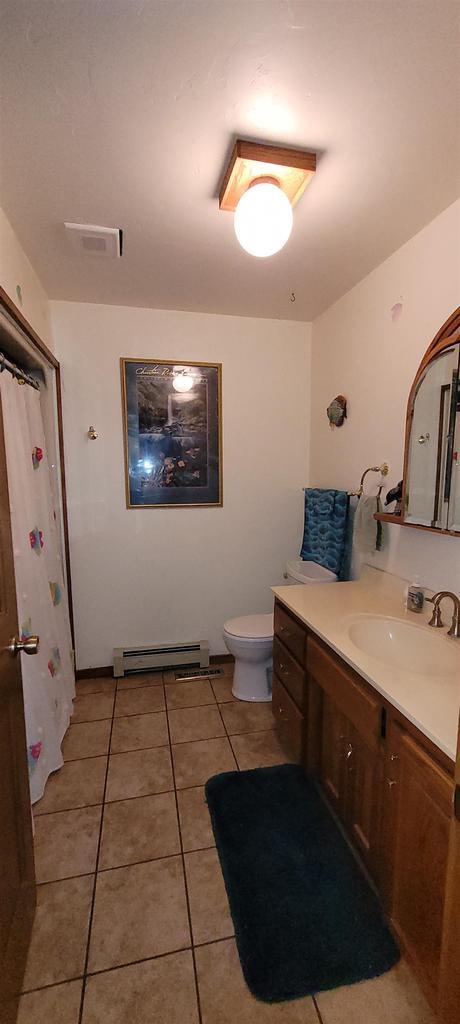 W6887 Two Mile Rd, Porterfield, WI 54159 - full bathroom featuring vanity, baseboard heating, tile patterned floors, toilet, and curtained shower