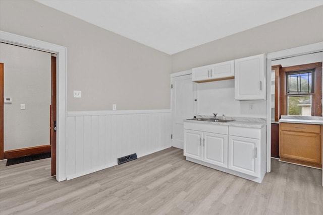 3046 N 57th St, Milwaukee, WI 53210 - kitchen featuring a wainscoted wall, a sink, light countertops, light wood finished floors, and white cabinets