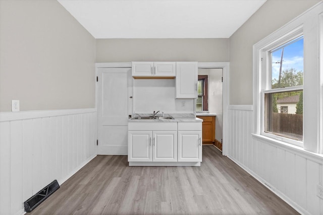 3046 N 57th St, Milwaukee, WI 53210 - kitchen featuring a wainscoted wall, light wood-type flooring, light countertops, white cabinets, and a sink
