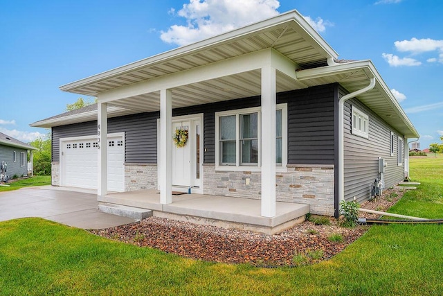 W4936 Battlestone Station Rd, La Crosse, WI 54601 - view of front of house featuring covered porch, concrete driveway, an attached garage, stone siding, and a front yard