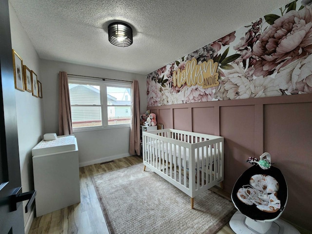 307 W Jackson St, Tomah, WI 54660 - bedroom with light wood-style flooring, a textured ceiling, a wainscoted wall, and a crib